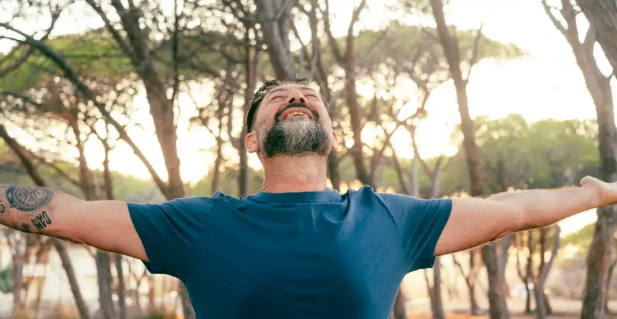 A man outdoors with arms open, finding relief in recovery